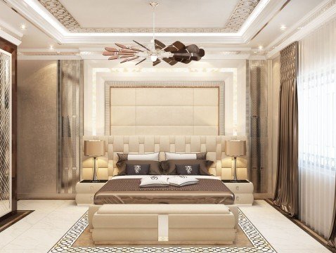 This is a picture of a modern, luxurious living room. It features a stylish, white-patterned wall backdrop, with several built-in shelves and cubbies to display various personal items. The furniture is made from white leather, with a large brown-patterned rug taking up the center of the room. A grand chandelier hangs from the ceiling, providing a dramatic, elegant touch to the room.