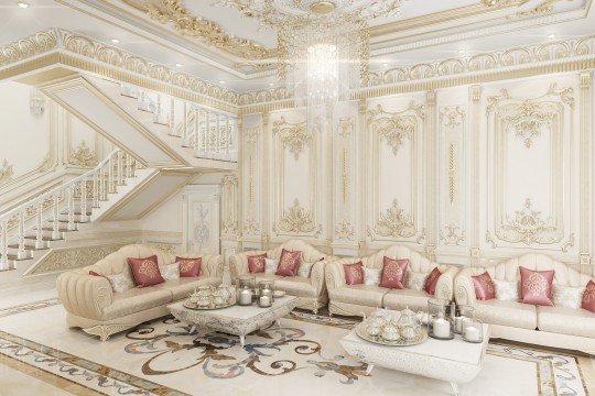 This picture shows an opulent living room with contemporary accents. The room has a large, luxurious, curved sofa upholstered in light pink velvet surrounded by two tall brass lamps on either side. The walls are painted an off-white color and feature a floor to ceiling built-in bookcase filled with books and decorative objects. The room also features a plush white rug and two armchairs upholstered in a beige textured fabric.