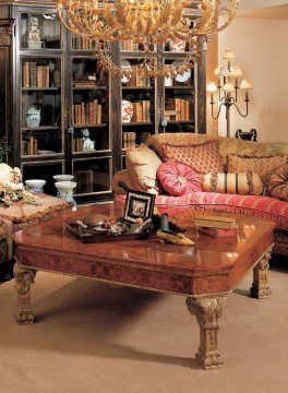 This picture shows a white and gold room in an elegant neoclassical style. The walls are filled with intricate Baroque-style stucco work, featuring ornate motifs, shells, and floral patterns. The furniture is also neoclassical in style, with classical details like gilded frames, cabriole legs, and carved embellishment. The room is lined with white columns, and a large window overlooks a garden.