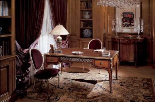 The picture shows a modern living room design with a large, open space and luxurious furniture. The room features a cream-colored velvet sofa, two matching armchairs, and a glass coffee table with gold legs. A white rug with an abstract pattern covers the floor, and there is a white shag rug in the center of the space. The walls are light gray and have a television mounted on them. The room also includes an illuminated aquarium, as well as several plants, giving it a calming ambiance.