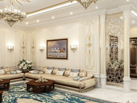 This picture shows a modern, luxury living room with a curved white sofa, a white and gold coffee table, and a black and gold wall panel behind it. On the right side of the room, there is a medium-sized screen TV mounted on the wall, along with several paintings and frames. In the center of the room, there is a beautiful crystal chandelier hanging down from the ceiling. The floors are a light marble, while the walls are a soft cream color.