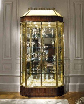 This picture shows a luxurious interior design with a large double door entrance. The walls are marble, and the floor is tiled with white marble. The doors are framed with gold detailed trim, and there is a large crystal chandelier in the center of the room. In the background, there is a large staircase, which is also tiled with white marble, and it leads up to an archway.