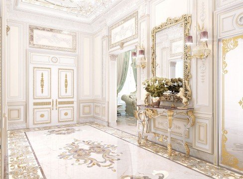 This picture shows an elegantly designed home interior. The walls are painted a light cream color with white accents. There is a large staircase in the center of the room, with a patterned carpet runner up the stairs. At the base of the stairs there is a chandelier hanging from the ceiling. On the wall to the left there are two framed pieces of art and a silver mirror. On the right side there is a built-in bookshelf filled with books, plants and décor. The floor is covered in a plush beige rug.