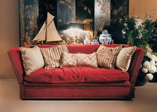 This picture shows a luxurious living room in neutral tones and a modern style. The walls are painted in a light beige color, and the floor is covered with a large beige rug. There is a white sofa set with a chaise lounge and two armchairs, and there are beautiful round armless chairs and a contemporary coffee table in the center. On each side of the sofa, there are stylish end tables with slim lamps, and there are also two tall wall sconces on either side of the entrance.