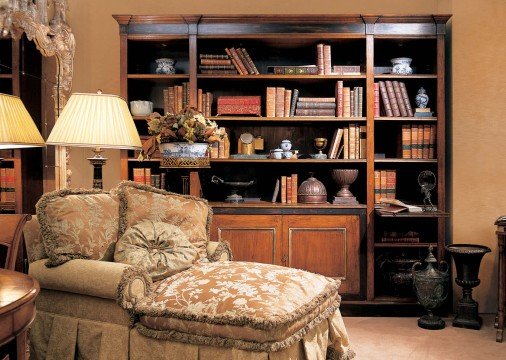 This picture shows a modern living room. The room is decorated with contemporary furniture, including a grey sectional sofa, a glass coffee table, and an area rug in shades of brown and beige. There is a wall art piece on one wall, and a large window overlooking the city skyline.