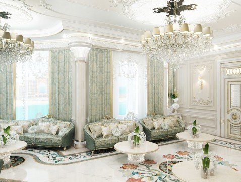 This picture shows a luxurious, modern living room. It features an off-white couch situated beneath two large windows that are framed with white drapes. There is a crystal chandelier suspended from the ceiling and there is a white and gold credenza against the wall. The walls are light grey with an intricate golden design. In the foreground of the picture is a round wooden coffee table with a vase of pink flowers on it.