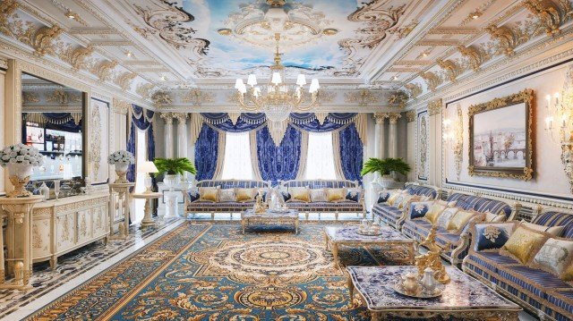 This picture shows an ornate, luxurious living room with a marble floor. The furniture is comprised of an ivory and gold sofa set, two white armchairs, and gold-accented end tables. The walls are painted cream and the ceiling is decorated with intricate gold moldings. A sparkling chandelier hangs from the ceiling, filling the room with light. At the center of the room is a beautiful, round ornamental rug in shades of blue, orange, and green.