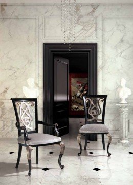 This picture shows an ornate hallway featuring a stunning marble floor, highlighted by intricate and colorful floral patterns. The walls are covered in luxurious velvet wallpaper with gold trim, and sconces lighting the way along the hallway. A cream colored chair sits at the end of the hallway, coordinating with the light color palette.