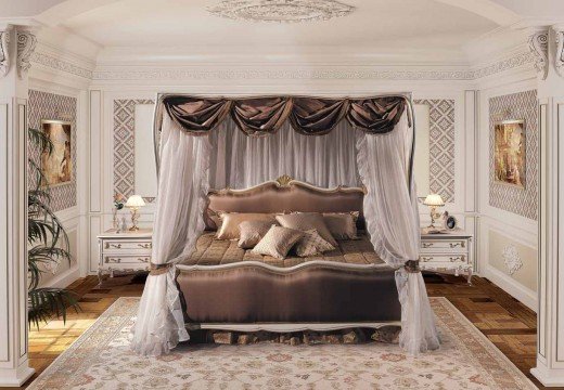 This is a picture of a modern bedroom with stylish décor. The room is mostly neutral in color, featuring light beige walls and white trim. There is a large bed in the center of the room, made of dark wood and topped with a white comforter, white and gold pillows, and several layers of blankets. To the left of the bed is a modern wooden dresser with a large mirror on top and two small nightstands. To the right of the bed is an upholstered chair and a floor lamp. The floors are contrasting, with dark hard