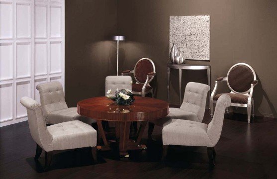 This picture shows a luxurious bedroom in a modern style. It features marble tile floors, a large mirror, and plush furniture in metallic colors. The walls are decorated with abstract art, and the bed is covered with a comfortable white duvet. A set of tufted chairs are placed in front of the bed, and luxurious curtains frame the windows.