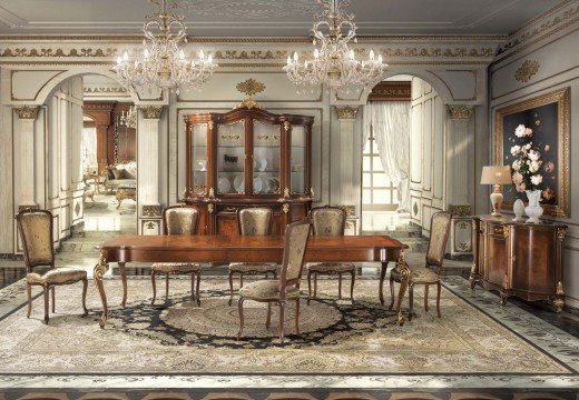 This picture shows a luxurious marble hallway with elaborate gold detailing. The walls are detailed with several sconces and a textured gold pattern. A large, intricate chandelier hangs from the ceiling and the floor is tiled in a complex pattern. The color palette is predominantly white and golden, with accents of beige.