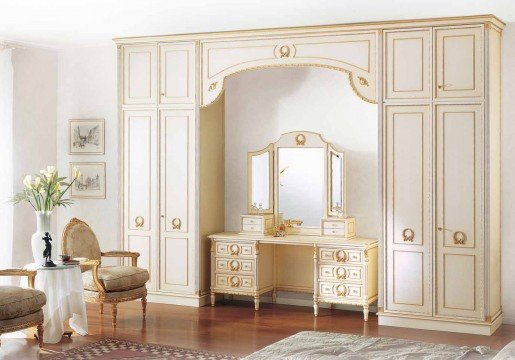 This picture shows a luxurious interior design, featuring a classic white marble entryway and a grand staircase with curved balustrades and ornate wood railings. The floor has intricate dark hardwood inlays and a beautiful crystal chandelier hangs from the ceiling. The walls are light grey and decorated with golden accents, large mirrors and small round sculptures. Above the stairs is an enormous classic painting of a view of a city.