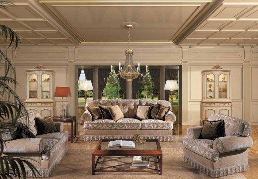 This picture is showing a modern contemporary bedroom. The room features a beige wall with a brown accent wall, black and white marble floors, and a light grey curved tufted headboard. A set of crisp white linens are draped over the bed and accent pillows in a variety of grey and white shades add texture to the space. The room also includes a white desk with a mid-century modern chair and a white nightstand. There's also an elegant crystal chandelier hanging from the ceiling.