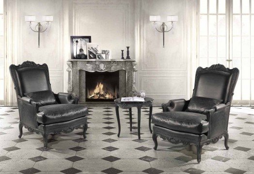 This photo shows the luxurious interior of a modern living room. The walls are painted in a light hue and the floor is a deep brown marble. There is a large area rug in the center of the room with several plush couches and arm chairs surrounding it. The left side of the room features a built-in bookshelf and a wall mounted television. A large crystal chandelier hangs from the ceiling and gives the room a soft and inviting atmosphere.