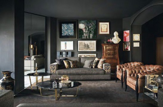 This picture shows a luxurious modern living room with a beige color palette. The room is furnished with a large cream-colored sofa, two chairs, and an ottoman. Large windows let in plenty of natural sunlight and reveal a stunning view of the pool and garden beyond. A black marble fireplace takes pride of place in the center of the room, and a grand chandelier hangs from the ceiling. A round glass coffee table with a matching side table, some lamps, and a decorative plant add to the room's sophisticated ambiance.