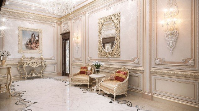 This picture shows an ornate, luxurious living room with an ivory color palette. It features a tufted cream sofa, two matching armchairs, and an ottoman upholstered in a geometric pattern with accents of black and gold. A large round chandelier hangs from the center of the room. The walls are adorned with elaborate crown molding, and the floor is covered by a plush white rug.