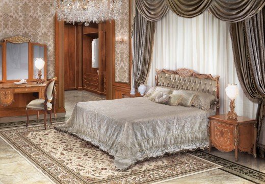 This picture shows a grand, luxurious bathroom in a modern style. The bathroom is spacious, with pale beige walls and a dark marble floor. In the center of the room, there is a large, round soaking tub set atop a raised platform. On either side of the tub are two open marble vanities with two vessel sinks, one on each side. There is a large shower enclosure with a panel of frosted glass doors, and a rain showerhead installed above the enclosure. On the left, near the window, there is a wall-mounted radiator, and to the right of