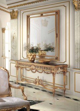 This picture shows a luxurious living room, with white furniture and accents of marble and gold. There is a white leather sofa across from a large gold-framed mirror and a white coffee table. The walls, floor and ceiling are decorated with black marble and dark wood panels, while two wall sconces provide additional light. The room also has several rugs and plants, adding a touch of color and life to the space.