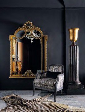 This picture shows a luxurious living room designed in a classic style. It features a large sectional sofa upholstered in a white and grey patterned fabric, with a patterned rug beneath it. A classic marble fireplace is framed by two wooden shelves on either side, each stocked with books and other decor. The walls are painted in a warm beige tone, and the floors are laid in dark hardwood. A crystal chandelier hangs from the ceiling, completing the elegant look.