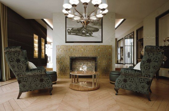 This picture shows an ornately decorated living room. It features a large white sectional sofa with gold accents and a black and white area rug. There is a large fireplace with a white marble mantle and two wooden armchairs covered in white and gray patterned upholstery. A crystal chandelier hangs from the ceiling, and two abstract paintings are hung on either side of the fireplace. The walls are a soft gray color, and several small sculptures and art pieces are displayed on the mantelpiece.