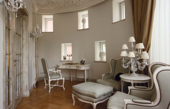 In this picture, we see a grand, luxurious living room. The walls have a fabric-style wallpaper in warm hues of orange, brown and yellow. In the center is a large, ornate sofa upholstered in a leopard print with large feather-filled cushions. A light-colored rug lays in the middle of the room with a small glass coffee table in the center. On the walls are two framed oil paintings and a sculpture of a horse. The overall effect is a very opulent and sophisticated living room.