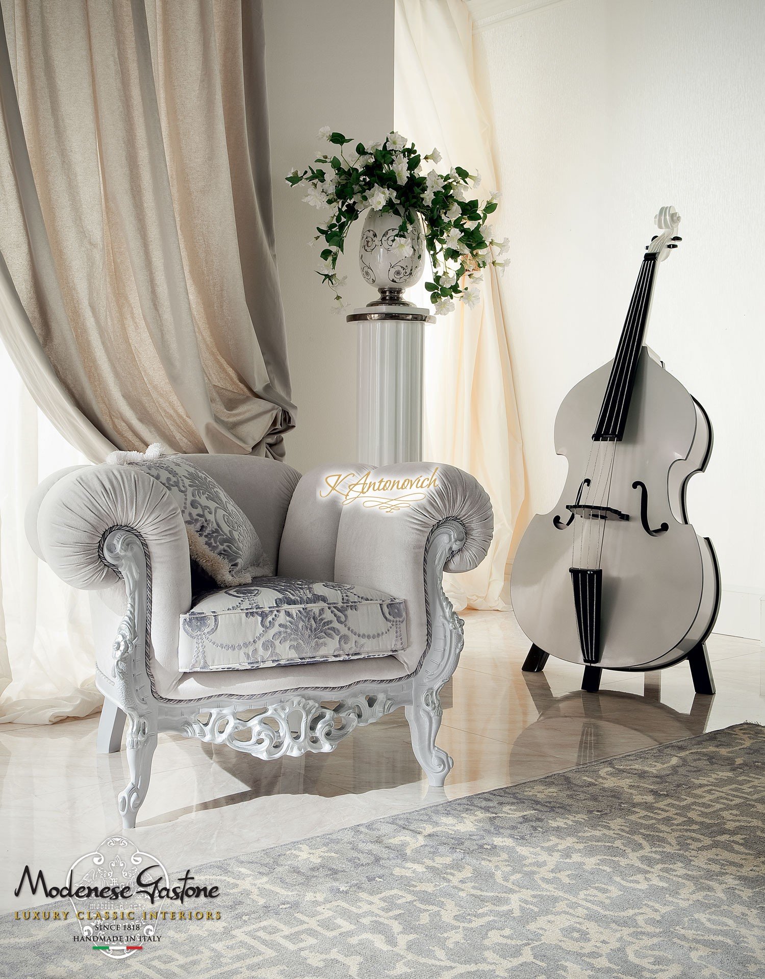 This picture appears to be an interior design featuring a modern living room. It features a white sofa with several colorful patterned pillows, two armchairs, and a large round coffee table. The floor is covered with a soft gray rug and the walls are a light gray color. On the walls, there are several framed pictures hung in an attractive arrangement. The room is accessorized with various decorative items such as vases, books, plants, and sculptures.