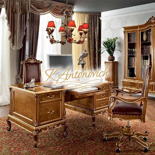 This picture shows a luxurious bedroom in an opulent home. The walls are cream colored, and the floor is tiled with a light beige marble. The bed is ornate and sits atop a raised platform. The headboard is upholstered in a golden fabric, and the bedding is covered with a plush comforter and several decorative pillows. On either side of the bed stands a white and gold nightstand with a unique glass table lamp on top. A large window allows in natural light, while two small white chandeliers hang from the ceiling.