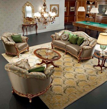 This picture shows an interior design of a modern living room. The room is decorated in shades of grey, white, and brown, with a beige carpeted floor. There is a large sectional sofa in the center of the room, facing an ornate fireplace. On either side of the fireplace are two glass-front cabinets, filled with books and decorative items. In front of the sofa is a coffee table, and against the walls are two end tables with small lamps. There is a large wall-mounted television to the left of the fireplace, and several framed artwork pieces hung around