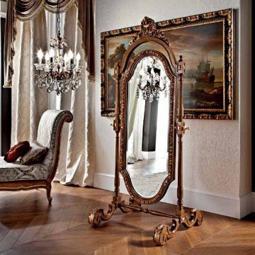 This picture shows a contemporary and luxurious interior design within a staircase area. The white walls and modern staircase railings stand out against the deep brown hardwood flooring. There is a light grey patterned rug visible on the stairs and various pieces of furniture on either side of the steps such as metallic chairs and a wooden bench. A unique chandelier hangs from the ceiling, adding a sophisticated touch to the overall aesthetic of the room.