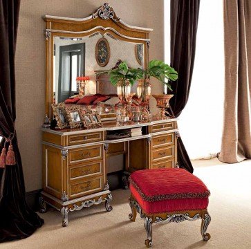 This picture shows a luxurious bathroom with an elegant marble countertop and two golden faucets. The room is decorated with a large mirror framed in gold trim, and a large window on the left wall gives a view of the outdoors. There are two shelves above the counter, one with white towels and one with candles. A single golden chandelier hangs from the ceiling, adding a touch of sophistication to the space.