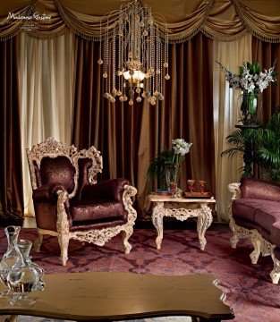 This picture shows a luxury bedroom design. There is a large bed in the center of the room, with two bedside tables on either side of the bed. The walls and ceiling are decorated with golden metal designs, and two large chandeliers hang from the ceiling. The walls are painted in a light beige shade, and there is an ornate wooden dresser in one corner. An open archway leads to another room in the background.