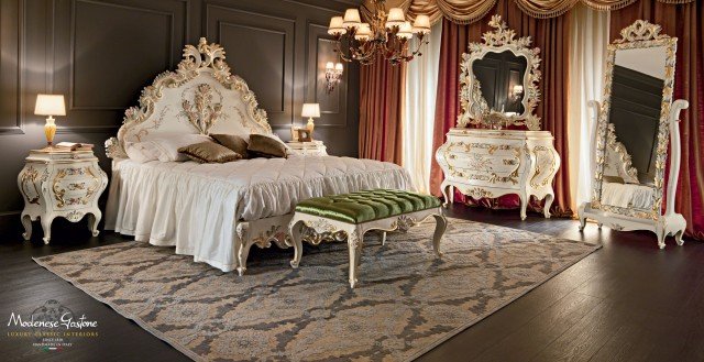 This picture shows a large, dark wooden table surrounded by six chairs. The chairs have high backs and are covered in a light grey fabric, a few of them featuring tufted buttons for a more ornate look. On the table is a floral center piece and several white plates and glasses.