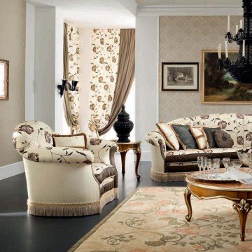 This photo shows a luxurious and modern living room. The room has several cream-colored sofas placed around a large square coffee table. Above the sofas is an intricate and sophisticated chandelier. In addition, there are two armchairs and several end tables placed on a light brown and patterned rug. A beautiful white grand piano sits in one corner of the room, and the walls are adorned with ornate and elegant wooden panels.