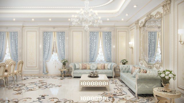 This picture shows a luxurious living room designed in an elegant modern style. The room is spacious and brightly lit, with a large off-white sofa and loveseat set off to one side. A polished white marble coffee table is situated in the center of the room, and two dark accent chairs flank it. There is a large area rug covering a portion of the floor, and a modern chandelier hangs from the ceiling. Along one wall there is a built-in shelf unit with mounted flat screen TV, and a fireplace below it.