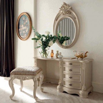 The picture shows an elegant open concept living room. The room features a high, vaulted ceiling painted with a white and gold pattern, and two of the walls are mostly glass, allowing plenty of natural light in. There is a grand white marble fireplace with a golden mirror above it, and there is a black leather sofa placed in the center of the room. On either side of the sofa are two unique armchairs with navy blue and white upholstery, and near the back of the room is a white grand piano. A round glass coffee table and large white fur rug add to the