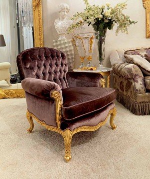 This picture depicts a modern and luxurious living room. The room features a large, light-colored sectional sofa, with large plush pillows for comfort. In the corner is an ornate gold and white armchair, and in front of the sofa, on a fur rug, is a low glass coffee table. The walls and ceiling are painted a light color, and feature contemporary lighting fixtures. A large flat screen television is mounted above the fireplace, and artwork hangs over the mantle.