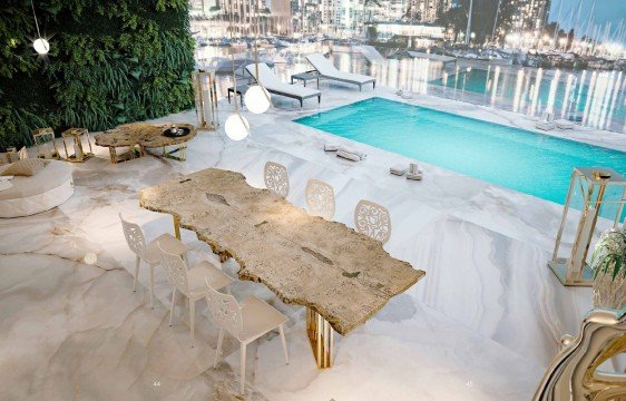 This picture shows a luxury living room. The room is decorated with white walls, crystal chandeliers, and rich wooden furniture. In the center of the room is an off-white sectional sofa, paired with two gold-accented chairs and a glass coffee table. A large rug covers most of the floor and is accented by two small side tables. On one wall is a large flat screen television and on another is a white grand piano.