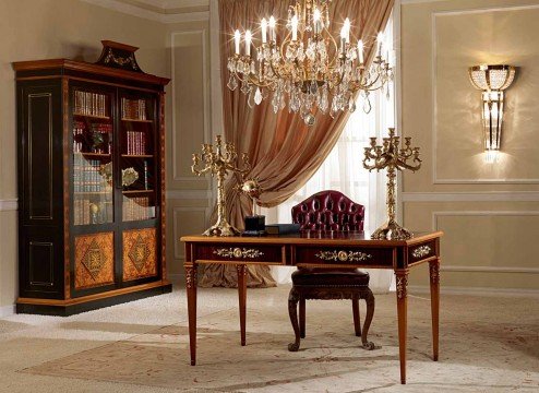 This picture shows a luxurious dining room with an ornate table, chairs, and light fixture. The walls are painted in a golden yellow tone and are adorned with intricate wallpaper. On the table is a beautiful floral centerpiece and dinnerware. The floor is covered with a luxurious area rug, and there are several drapes and curtains hung on the windows.