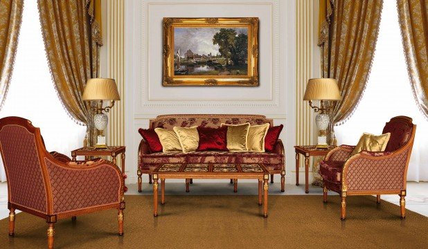 This picture shows an ornately decorated living room with a mix of modern and traditional design elements. The walls are painted a light pink color, with white crown molding and trim work. The floor is made up of patterned ceramic tiles with large rugs covering portions of the floor. The furniture includes a two-seater couch with decorative cushions, two armchairs, two ottomans, and a glass coffee table. On either side of the seating area are matching white bookshelves filled with books and decorative items, and a sideboard with a decorative mirror hangs on the