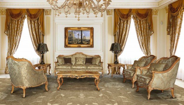 This picture shows an ornately decorated residential foyer with a marble floor and several pieces of furniture in it. The walls are painted beige and adorned with a few paintings, and there is a large staircase that leads up to a second floor. There is also a large chandelier hanging from the ceiling and two arched doorways leading off to other rooms.