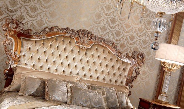 This picture shows a luxurious living room decorated with modern and contemporary design elements. The walls are painted in a pale blue color and the flooring is a cream-colored tile. The furniture is mostly white, with a black velvet tufted sofa and two matching armchairs. The center of the space features a crystal chandelier, along with a stone fireplace and an extravagant glass wall that serves as a room divider. A white curved staircase leads to the upper floor, while the pale blue walls are adorned with beautiful paintings.