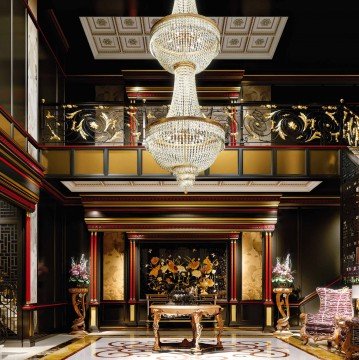 This picture is of a luxurious living room design featuring beige walls and high ceilings, a white marble fireplace with a flat-screen television mounted above, and a velvet tufted sofa in the center of the room. The room also features two armchairs in beige, a brown leather ottoman, and a glass coffee table with a marbled top. There are floor-to-ceiling windows that overlook a lush outdoor space, and a set of stairs leading to a second level.