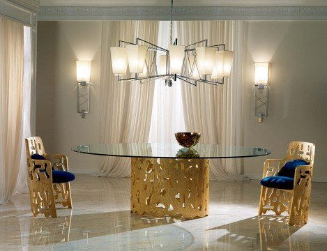 This picture shows a large, luxurious living room with light-colored walls and floors, patterned area rug, and several plush chairs and sofas upholstered in deep blue fabric. The room also features a fireplace, built in shelves, glass coffee table and window treatments that tie the look together. There are several pieces of artwork on the wall, and an arched doorway leading out into another room.