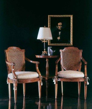 The picture shows a luxurious living room with ornate furniture, featuring plush white sofas and armchairs along with a wooden coffee table and side tables. The floor is covered in a rich patterned rug and the walls are adorned with artwork and gilded mirror frames. A large crystal chandelier hangs from the ceiling and provides a touch of glamour to the space.