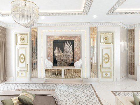 This picture shows a luxurious living room with a beautiful white and gold interior. The walls are painted in a soft white color and the room features a large white sofa, two white armchairs and a round gold mirror. There is also a white fireplace, an intricate chandelier, and two small black side tables with gold accents. The room is decorated with various ornaments, framed art and faux plants.