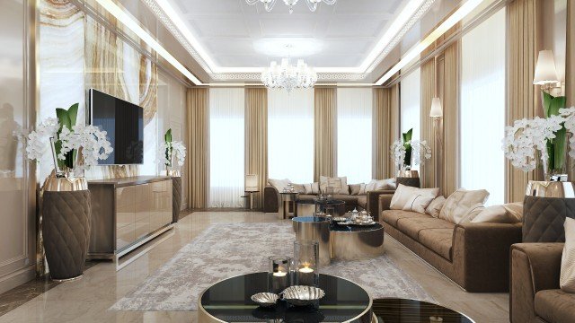This picture shows a lavish, modern living room designed in a white and gold color palette. The walls feature large windows draped in elegant sheer curtains, while the floor is covered in a plush white carpet. An ornate crystal chandelier hangs from the ceiling, illuminating the floating sofa and armchairs in the center of the room. On either side of the sofa, luxurious gold tables are filled with delicate decorative pieces. Gold accents also line the mantle of the fireplace in the back of the room, providing added sophistication to the space.