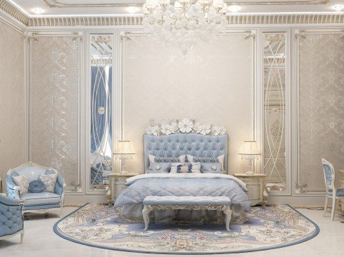 The picture shows an elegant upholstered headboard in a master bedroom suite. The headboard has a tufted design with a light blue and white fabric and finished with silver-tone studs. The overall design is a modern take on traditional style. It is accompanied by a matching, tufted bed frame complete with rolled edges. On either side of the bed are two end tables with lamps, providing a soft, ambient lighting.