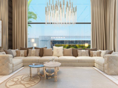 This picture shows a luxurious living room with modern furniture and sleek, contemporary design elements. The room features a pale grey sectional sofa, a matching armchair, two round black tables on each side of the sofa, and a set of glass doors leading out to a patio or balcony. The walls are painted a light grey color, and two large windows allow for plenty of natural light. A crystal chandelier hangs over the room, and several abstract paintings add a touch of flair to the space.