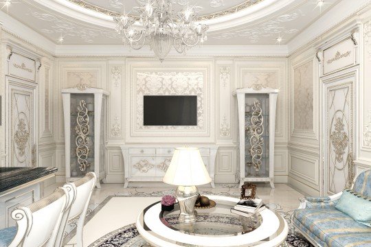 This picture shows a luxurious living room designed in a contemporary and classical style. The room contains sophisticated décor, such as a plush ottoman in a beautiful white-and-gold patterned fabric, a grand sofa upholstered in a white and gold velvet, a classic wooden coffee table, and a large mirror with gold leaf details. There are also two crystal chandeliers hanging from the ceiling, adding a touch of glamour to the room. In the background, there is an ornate staircase with wooden steps, metal railings, and cream-colored walls with a