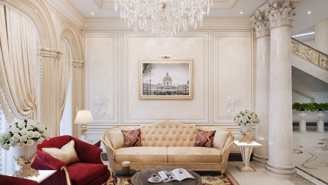 This picture shows a luxurious dining area with large crystal chandelier, white marble flooring, and a grand table surrounded by gold chairs. The centerpiece of the room is an intricate stone wall which is decorated with ornate carvings and a designer mirror on top. There are two small decorative side tables on either side of the table and a potted plant in one corner. The room also features colorful draperies, elegant lighting fixtures, and rich wood furnishings.